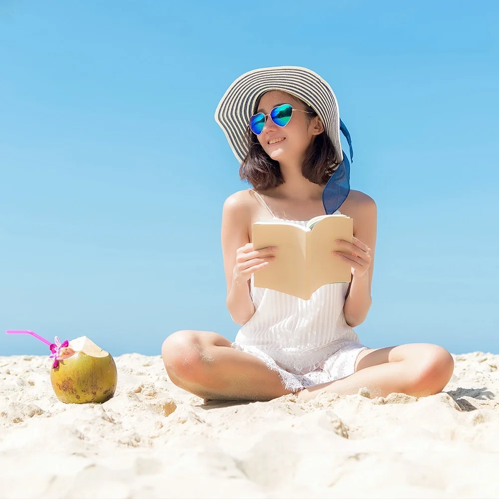 Original beach photo with a woman reading and a coconut drink in the sand beside her