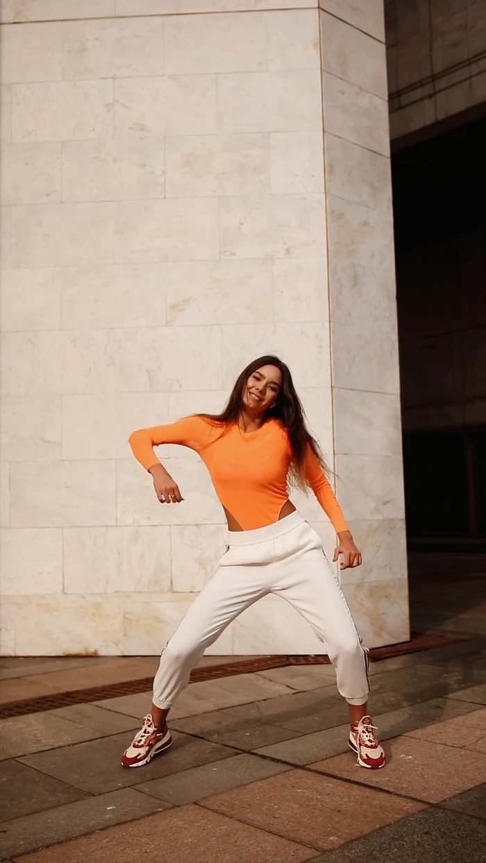 A frame from the original clip showing a woman dancing in an orange top and white joggers