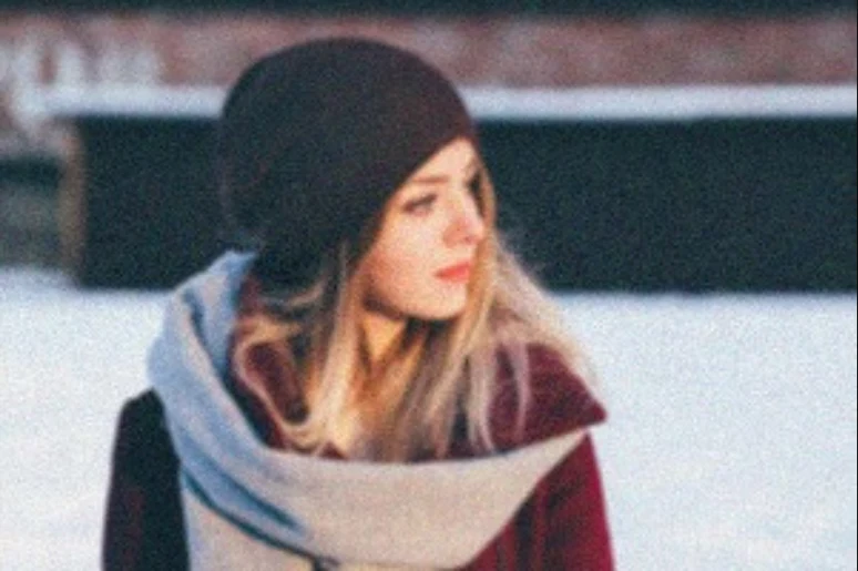 A grainy, blurred photo of a woman in a dark beanie and scarf against snow