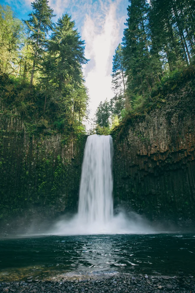 A still photograph of a waterfall falling into a pool between mossy cliffs