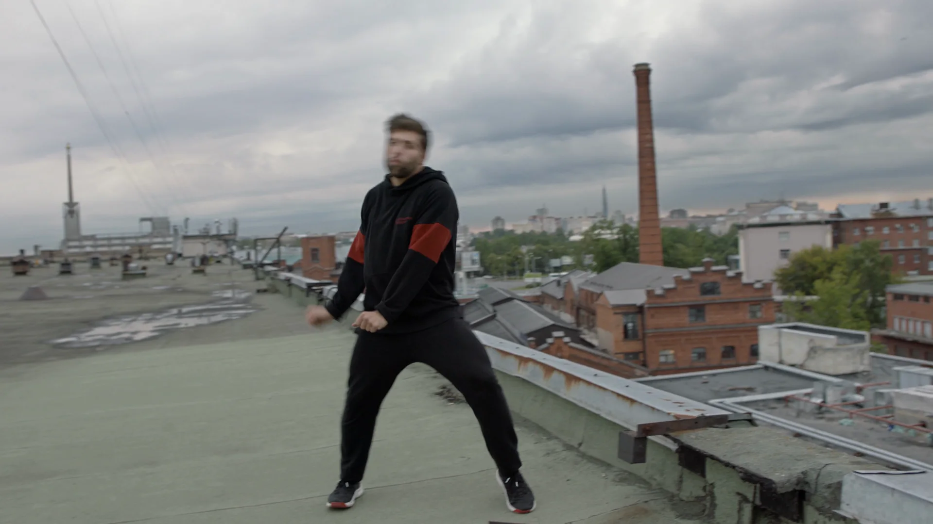 A dancer on a gray, overcast city rooftop, the frame flat and dim