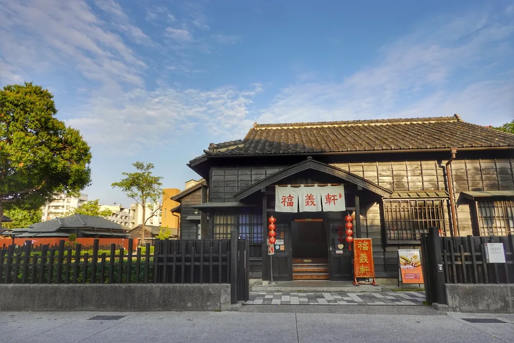 A traditional wooden building with a deep tiled roof, photographed from the street on a clear day.