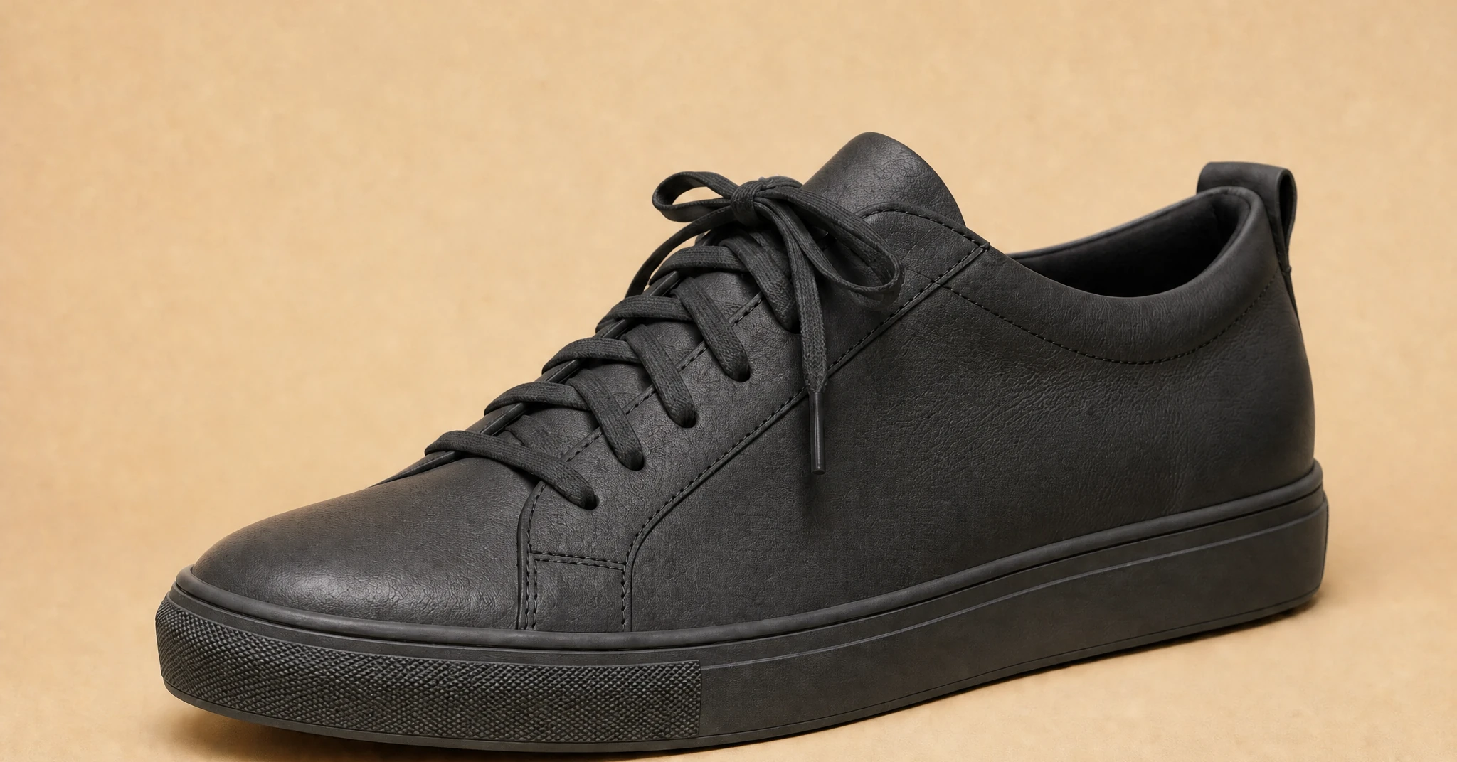 A plain product photograph of a black leather sneaker on a beige background, one of the four shots handed to AI Marketing Advisor.