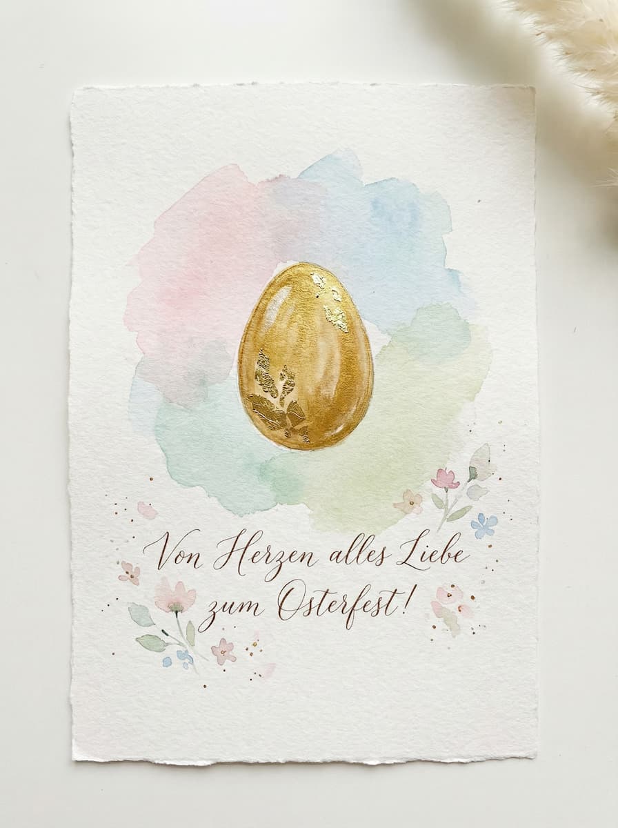Eine dekorative Osterkarte mit einem goldenen Ei in der Mitte, umgeben von zarten Pastell-Aquarellfarben und floralen Illustrationen. Der Text Von Herzen alles Liebe zum Osterfest! ist elegant in die Gestaltung integriert.