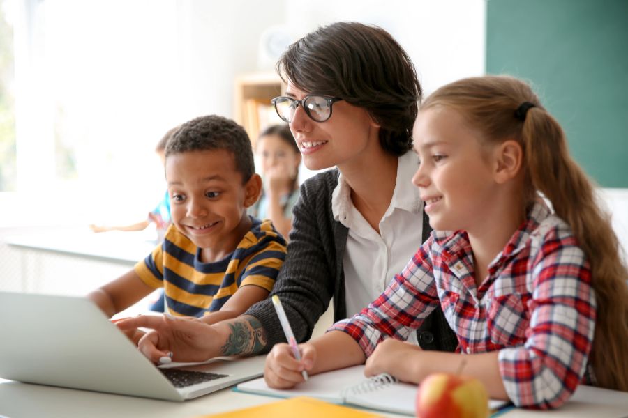 Female teacher helping two students learning using a laptop