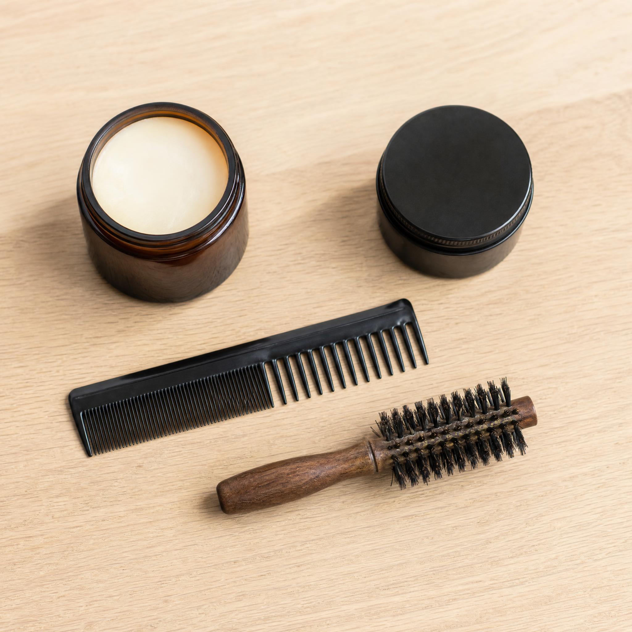 Bodegón de productos para peinar pelo corto: cera mate, pomada, peine de barbero y cepillo redondo