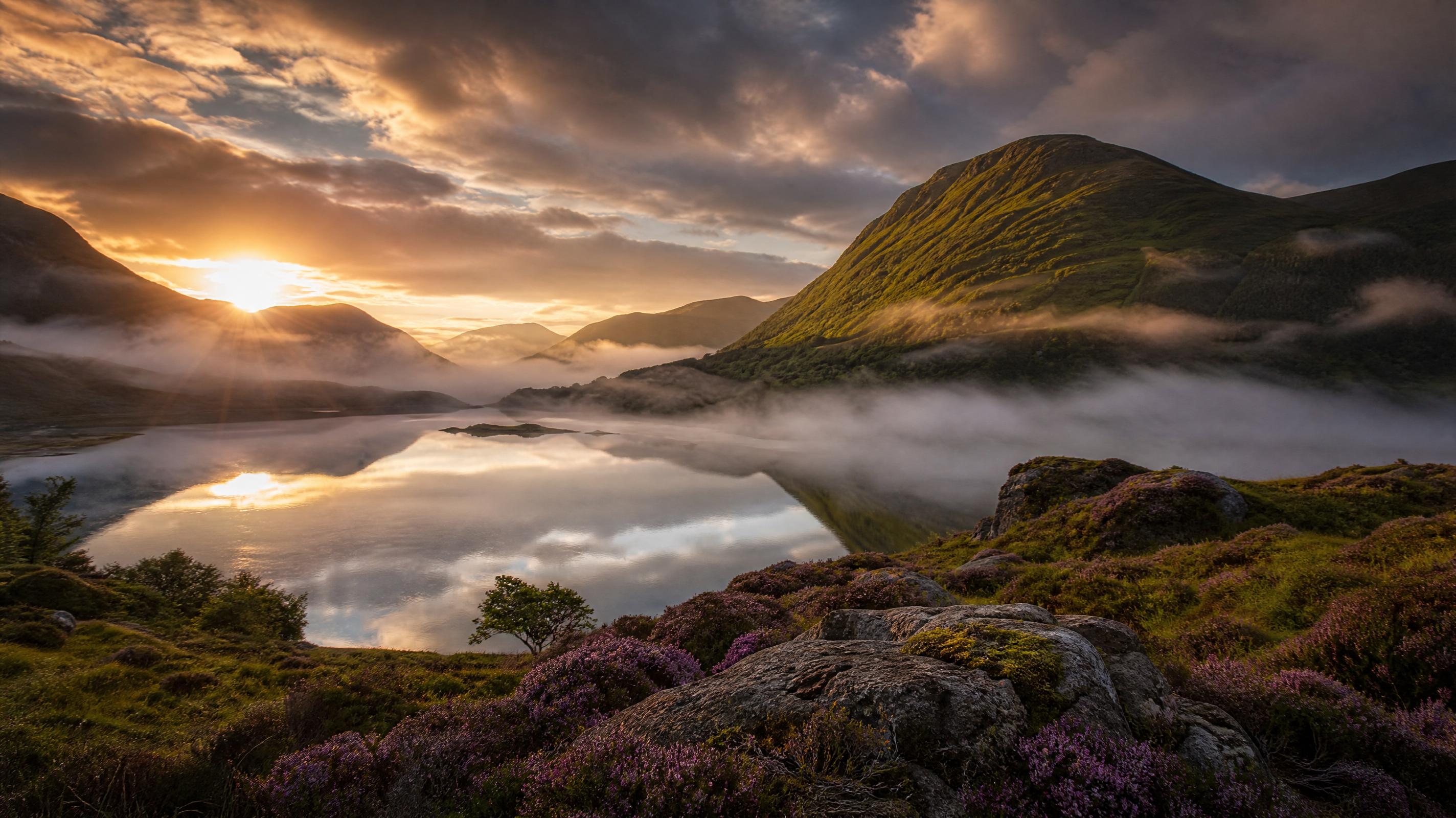 Paisaje panorámico de montañas escocesas al amanecer con niebla baja sobre un lago
