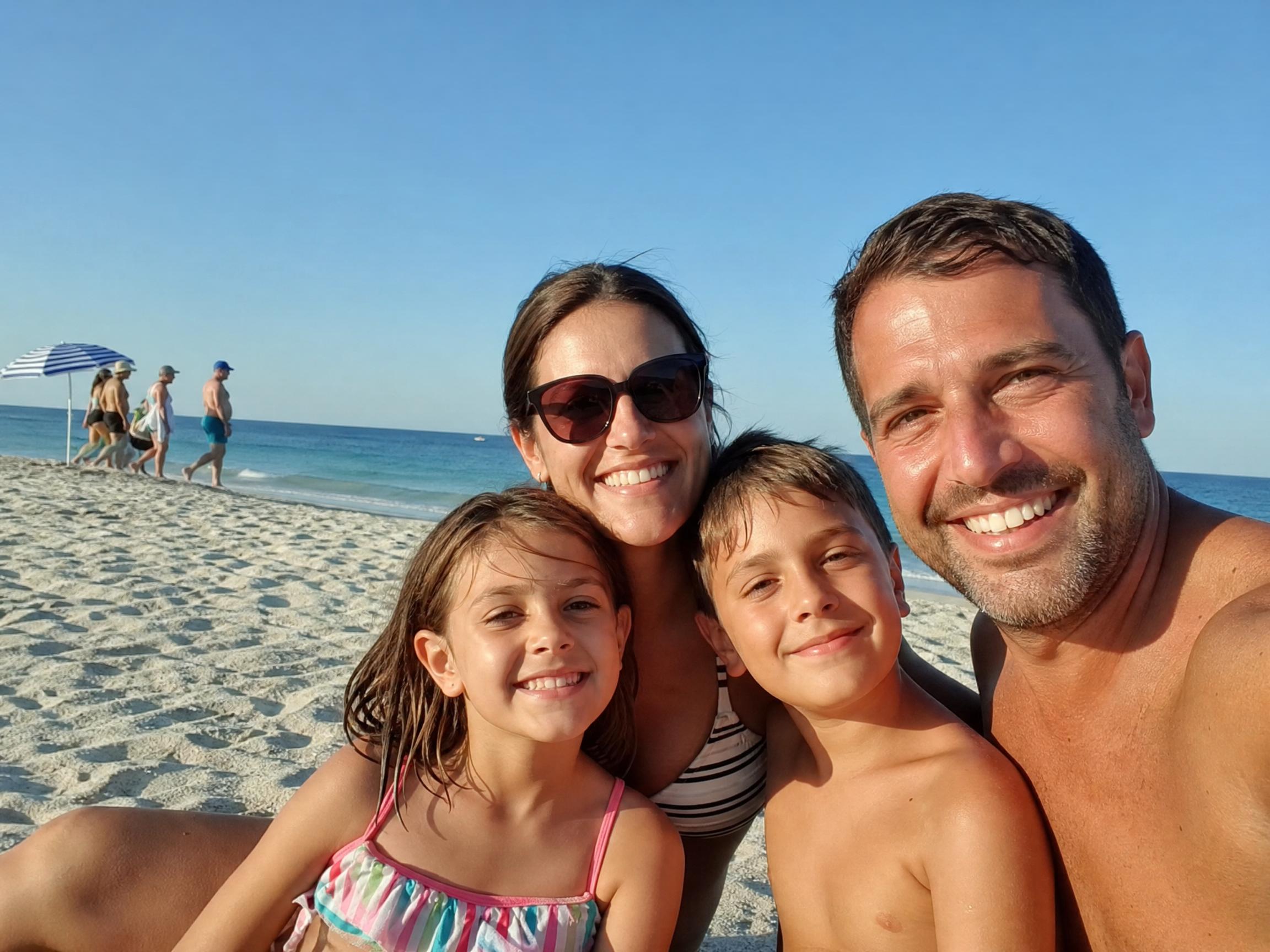 Antes: familia posando en la playa con varios turistas visibles al fondo a la izquierda