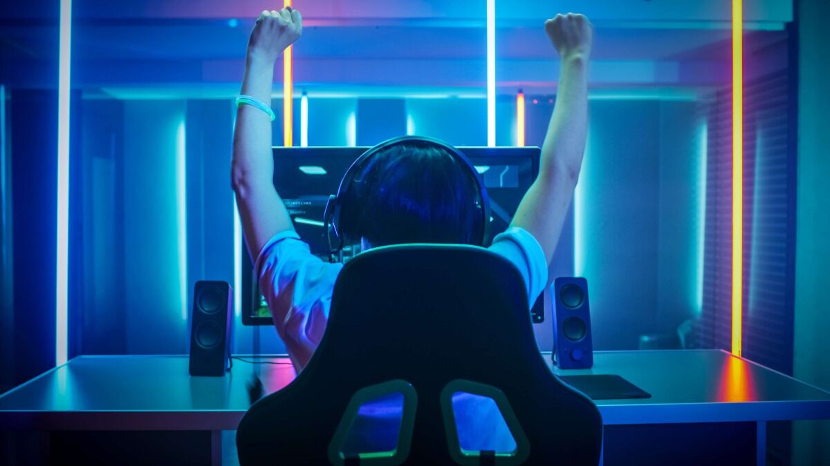 Gamer mit Rücken zugewandt vor Monitor reißt die Hände in die Höhe