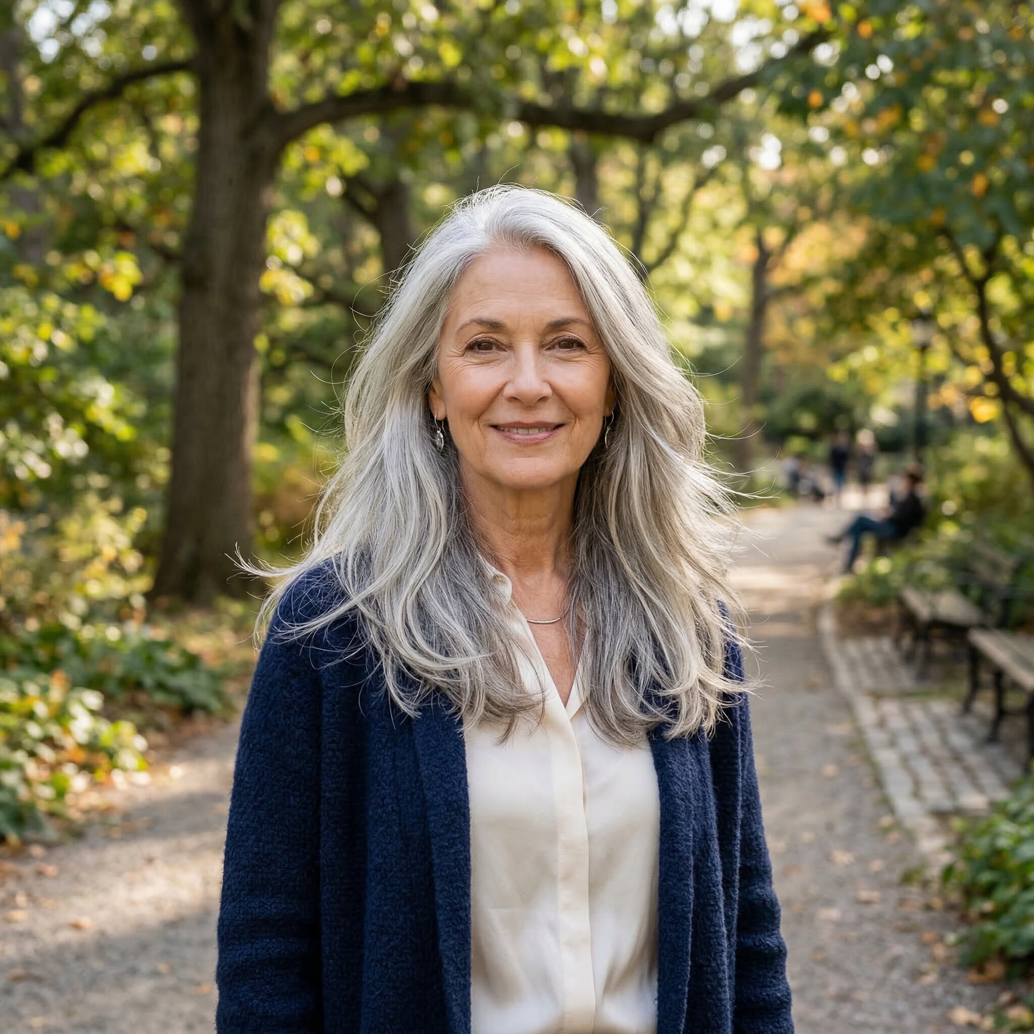 Woman with long layered silver hair flowing past shoulders, soft natural movement, outdoor park with sunlight, elegant realistic portrait
