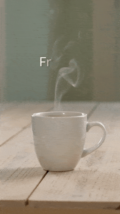 Ein animiertes GIF im Hochformat zeigt eine weiße Kaffeetasse auf einem hellen Holztisch, aus der sanft heißer Dampf emporsteigt. Im Hintergrund blendet sich im Verlauf der Animation der Text Frohen Montag in klarer, weißer Schrift ein.