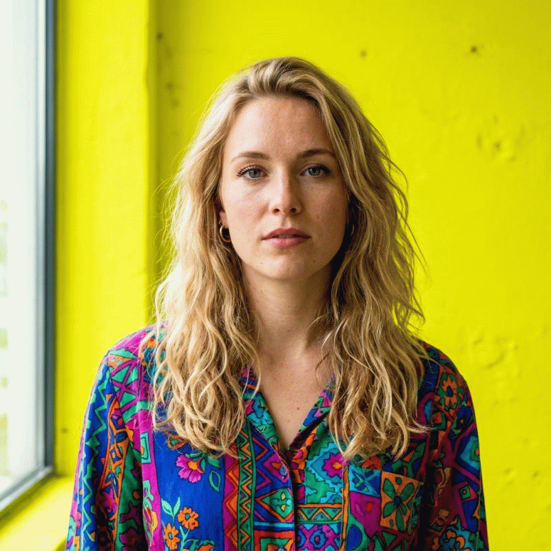 Ein Porträt-Beispiel, bei dem der knallgelbe, unruhige Hintergrund durch KI-Bildbearbeitung sauber und harmonisch umgefärbt wird. Lockige Haare und Kleidung bleiben perfekt erhalten.