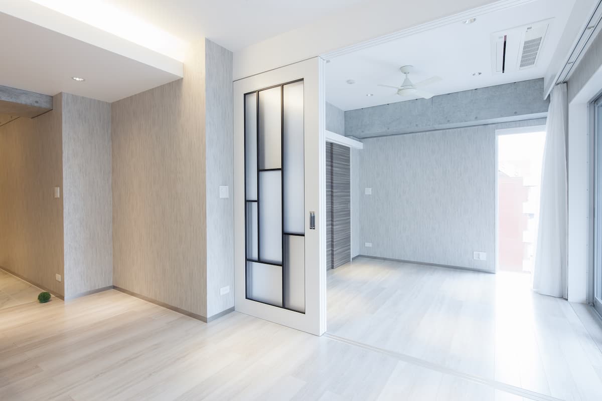 Ein leerer, modern gestalteter Raum mit hellem Laminatboden, weißen Wänden und einer gläsernen Schiebetür im minimalistischen Design.