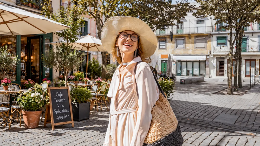 The same woman and pose, with a sidewalk cafe, outdoor tables, and flower pots where the tram was