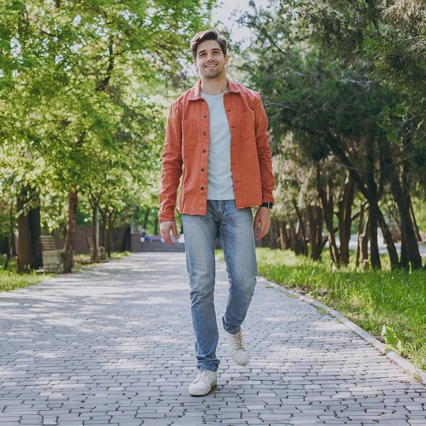 A man in an orange overshirt walking down a tree-lined park path, in full color