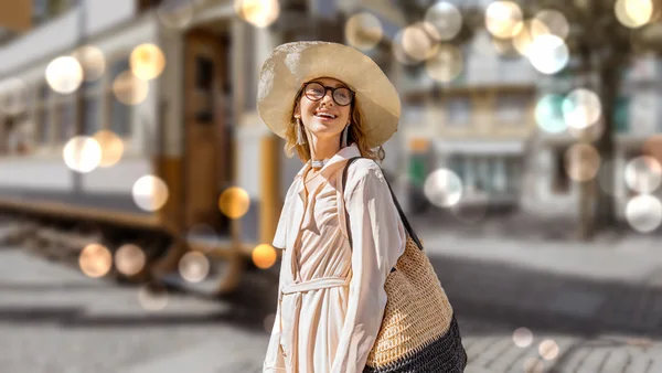 The same photo with the woman sharp and the tram and buildings blurred behind her, dotted with round lights