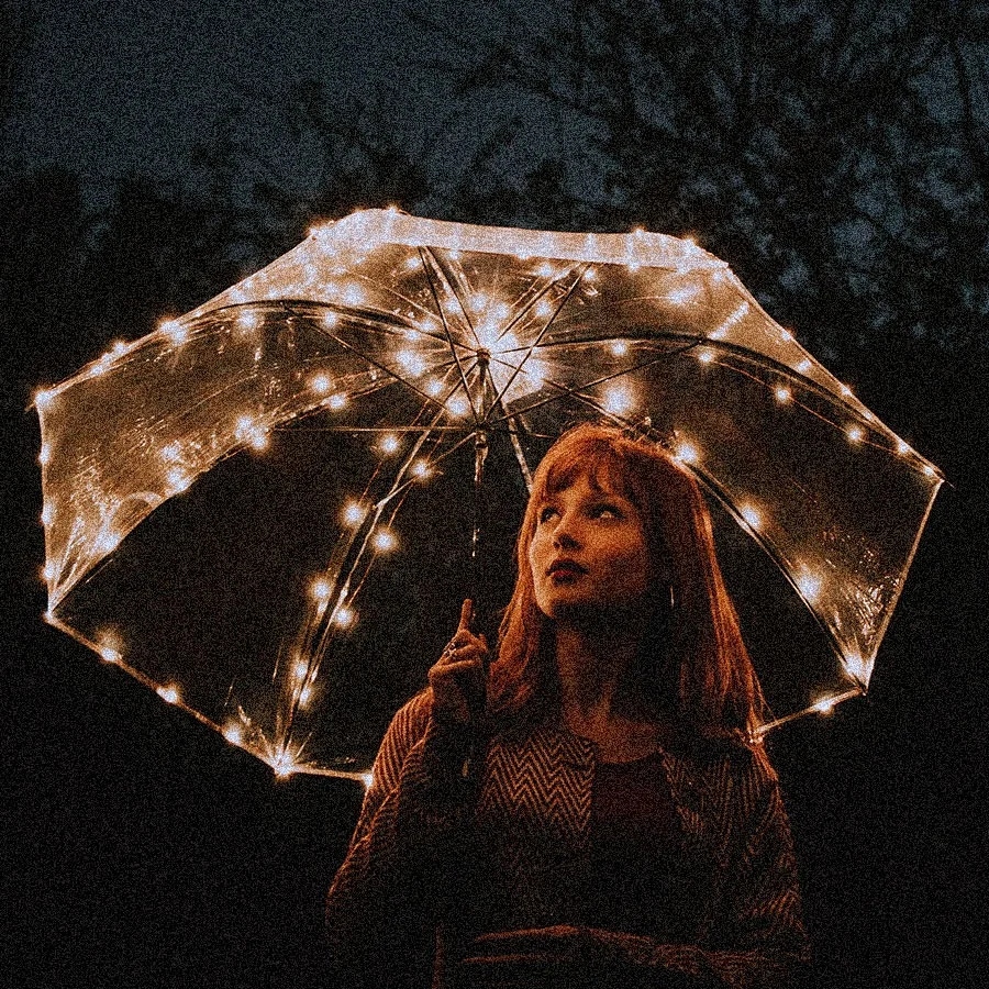 A woman at night under a clear umbrella strung with small lights